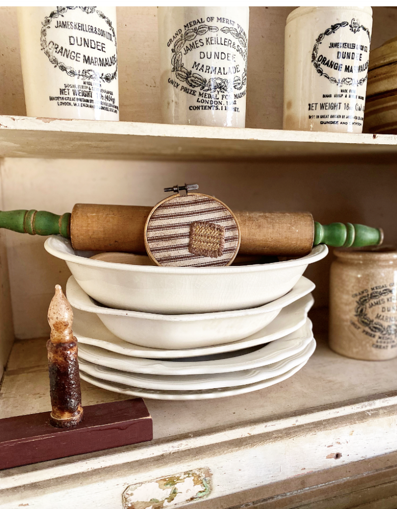 a rolling pin with green handles and a primitive hoop with a patch on a stack of ironstone
